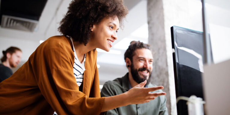 Two coworkers smiling while collaborating at a computer