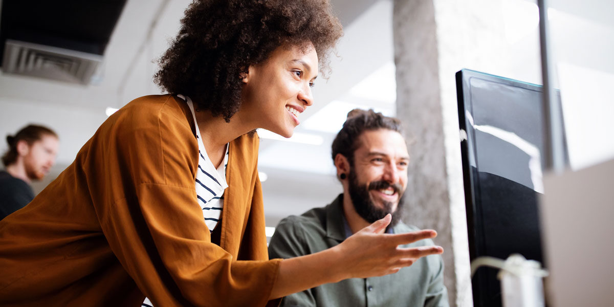 Two coworkers smiling while collaborating at a computer