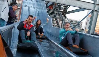 Four adults laughing and cheering on an outdoor slide
