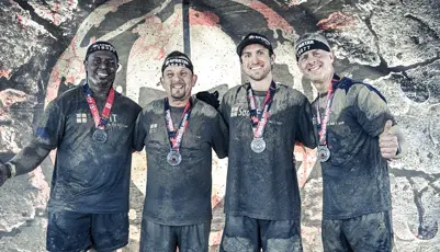 Four muddy men celebrating with Spartan Race medals