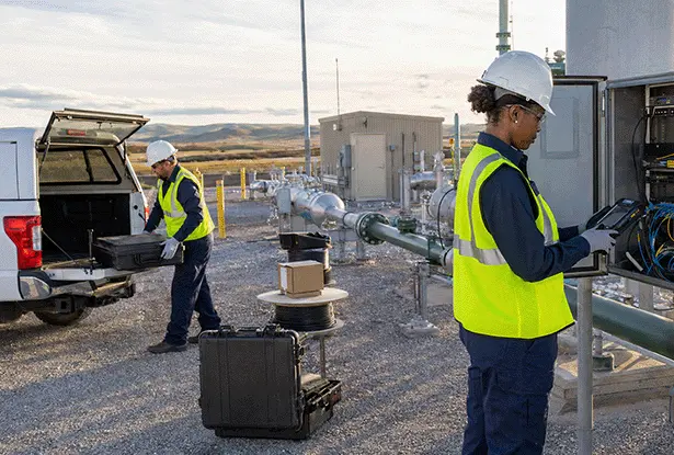 Two technicians working at an outdoor industrial pipeline facility